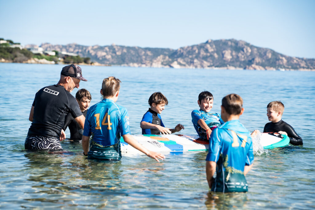 a group of children and instructor playing in the water with a surf board